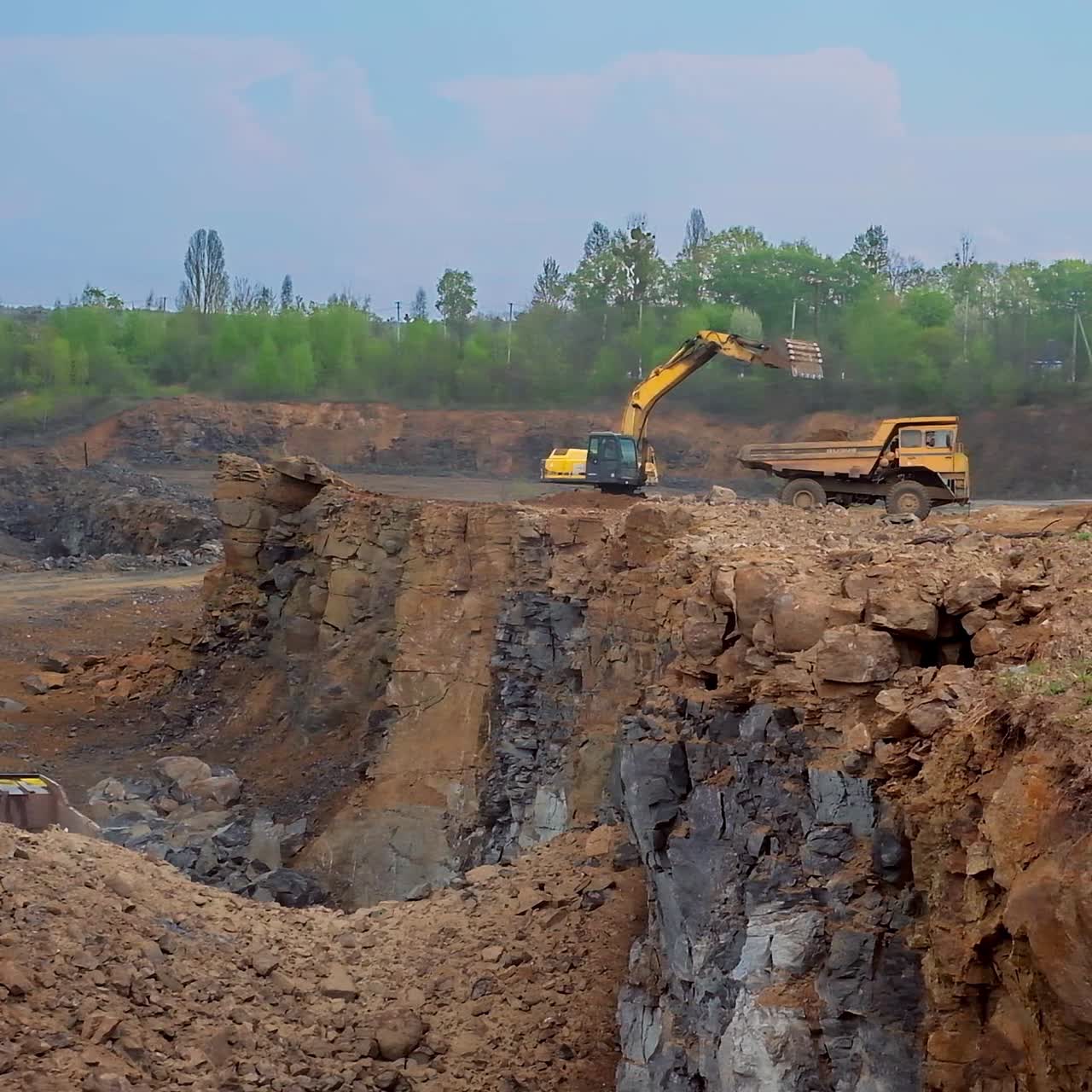 Tractor bucket is filling a truck. Industrial excavator loading soil on a truck on nature background. Earth moving equipment.