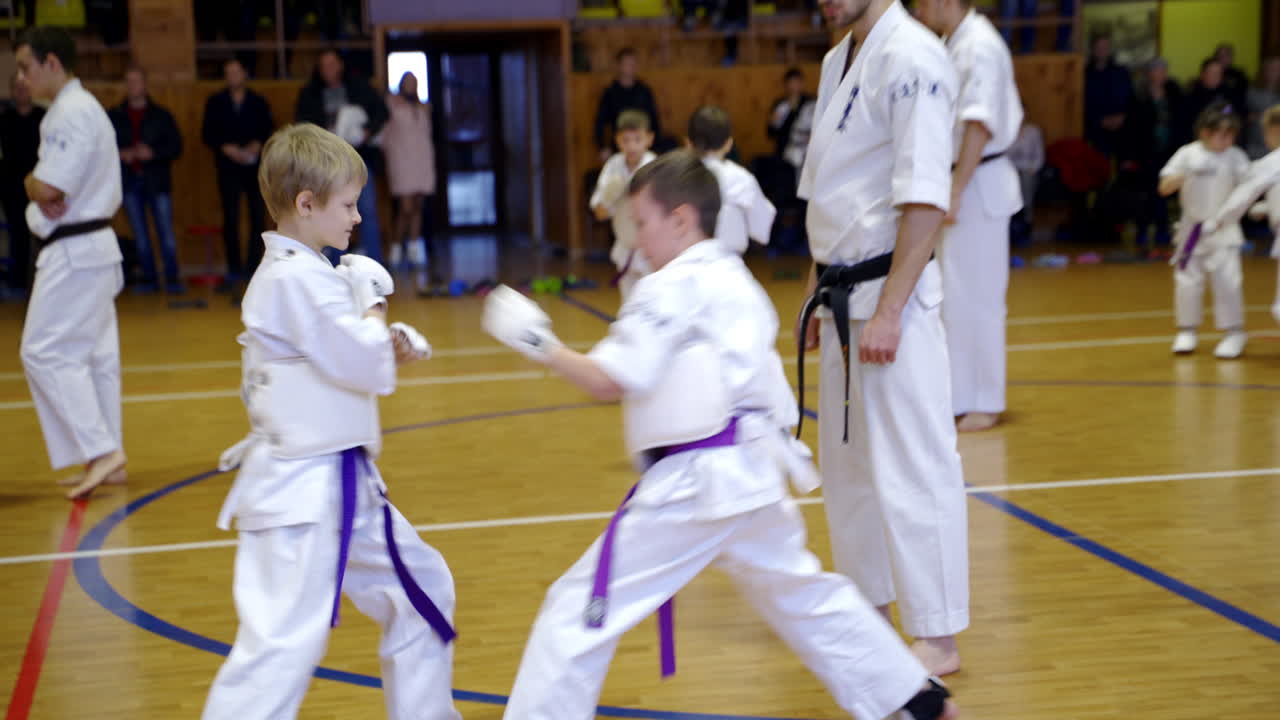 Young athletes sparring supervised by adult trainers. Boys divided into pairs to practice karate moves.