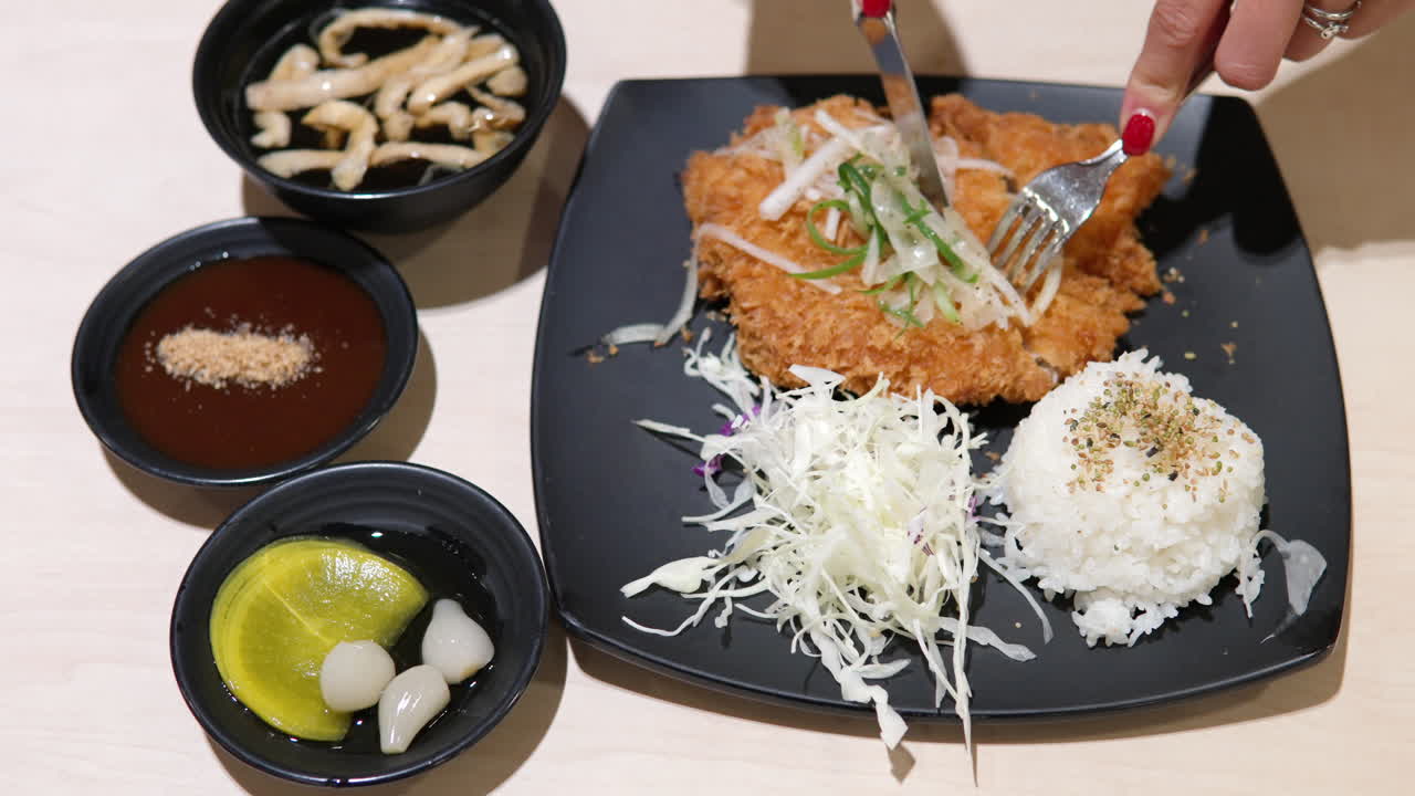 Woman's Hands Cutting Korean Chicken Tonkatsu Cutlet - top view