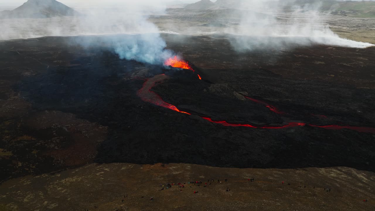 vista aérea del paisaje de personas que miran la erupción volcánica en litli-hrutur, islandia, con lava y humo saliendo