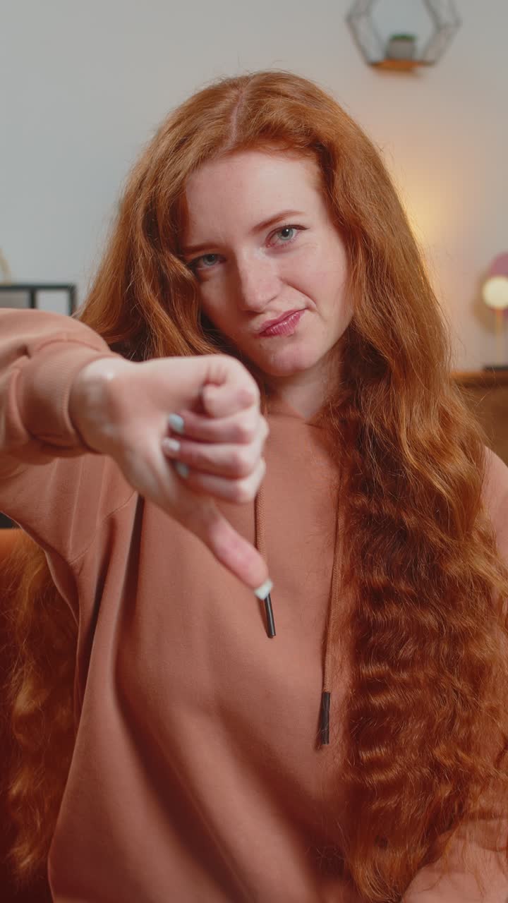 Upset woman showing thumb down sign gesture expressing discontent sitting on sofa couch at home