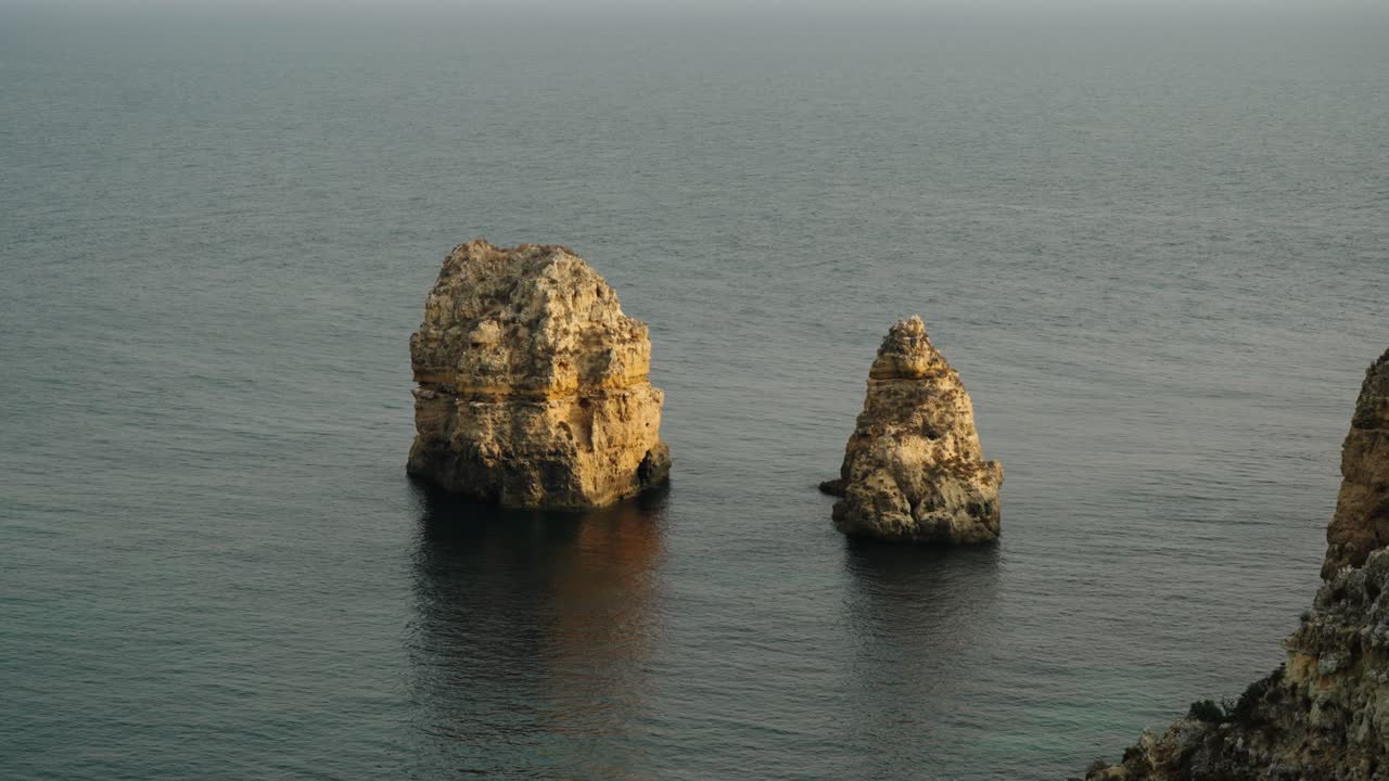 Kalkstenshavstakke rejser sig fra det rolige vand langs den naturskønne Algarve-kyst i Portugal