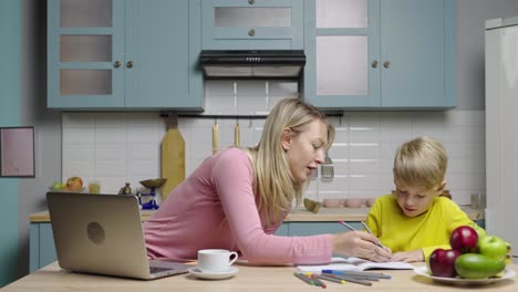 mother helps her son with his homework in the kitchen.