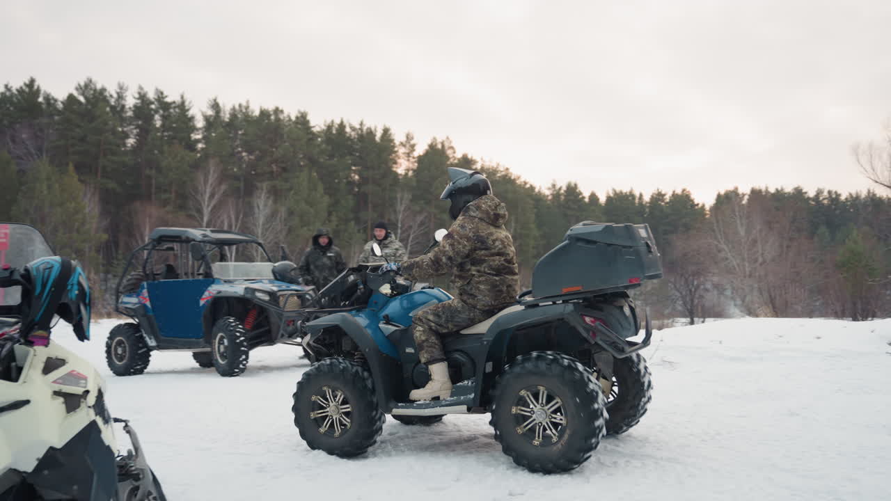 Piloti di quad nella foresta innevata che preparano l'attrezzatura, una squadra mimetica ispeziona i veicoli e le mappe, convoglio di quad al minimo su un campo ghiacciato, sfondo di pini e betulle, tracce fresche nella neve, tensa attesa prima dell'impresa estrema