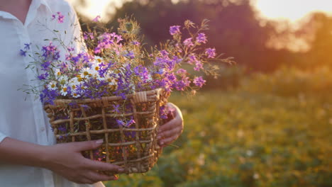 woman walks in a field with a basket of wild spring flowers