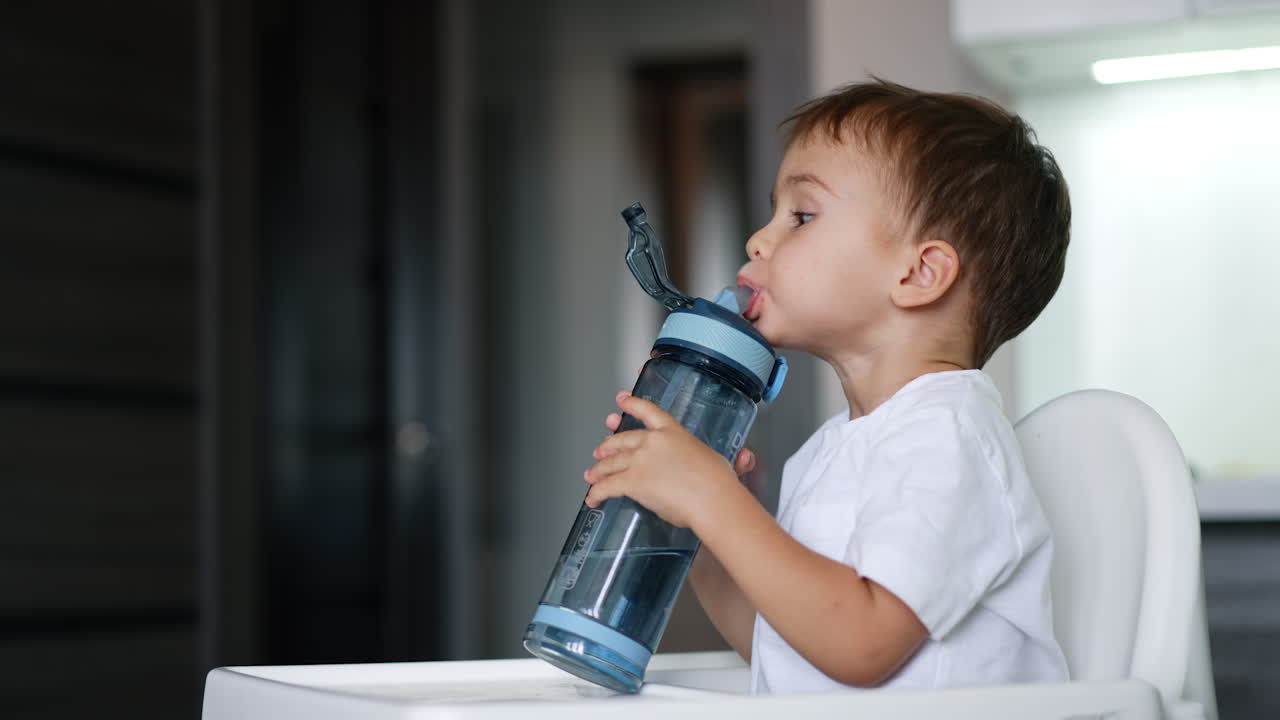 Lovely kid drinking water from a sport bottle. Cute toddler looks at camera, laughs and closes the bottle cap.