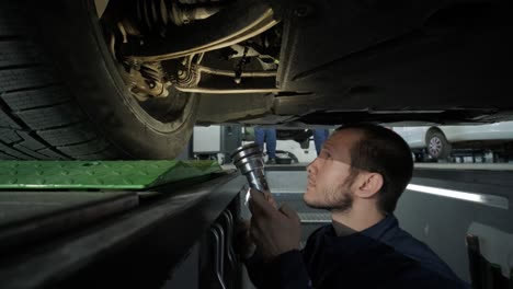 mechanic inspecting car undercarriage in service pit