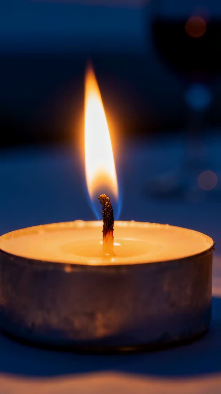 Video verticale: Candela tealight che si affievolisce mentre lo stoppino si carbonizza e la cera si accumula su un tavolo poco illuminato.