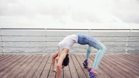 athletic young woman back bending and stretching on the beach by the ocean. crab position. slow motion shot