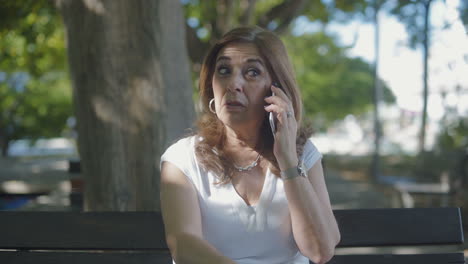 Elegant-middle-aged-woman-sitting-outside,-talking-on-phone