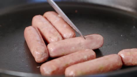 metal spatula turning and flipping breakfast sausages in hot cast iron skillet with oil splatters and steam in slow motion