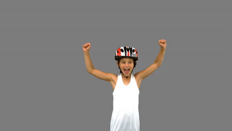 chica linda con un casco de bicicleta y levantando los brazos en la pantalla gris