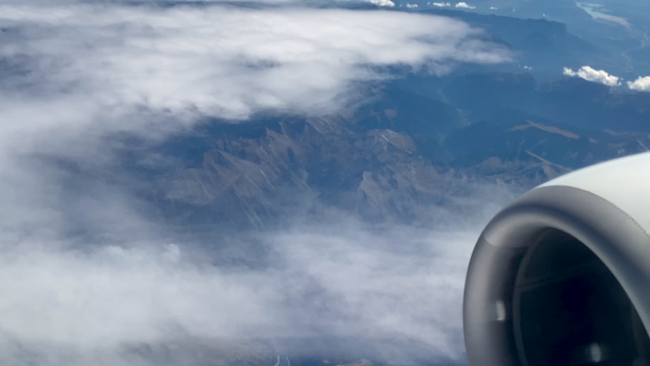 A bird's eye view of the turbine engine and the cloud-covered landscape from behind the airplane window