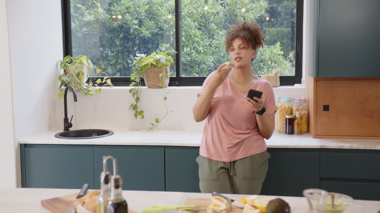 Mangiare uno spuntino sano, donna che usa lo smartphone in una cucina moderna