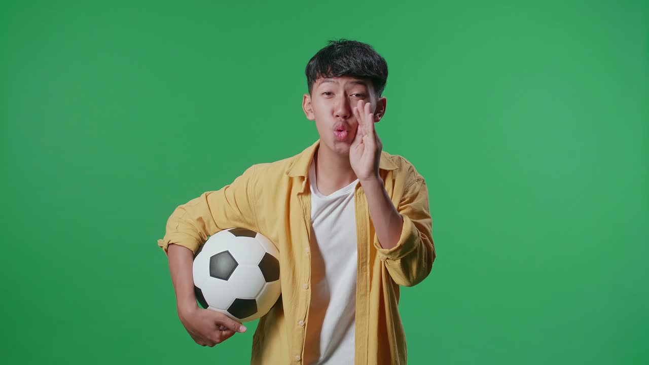 공을 들고 있는 아시아 소년은 초록색 스크린 배경에서 축구를 응원하면서 패배자들을 조롱하고 있다.