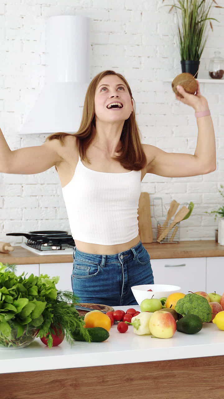 Funny and joyful girl dancing in the kitchen with fresh fruits in her hands. Good morning mood, healthy diet. Vertical video