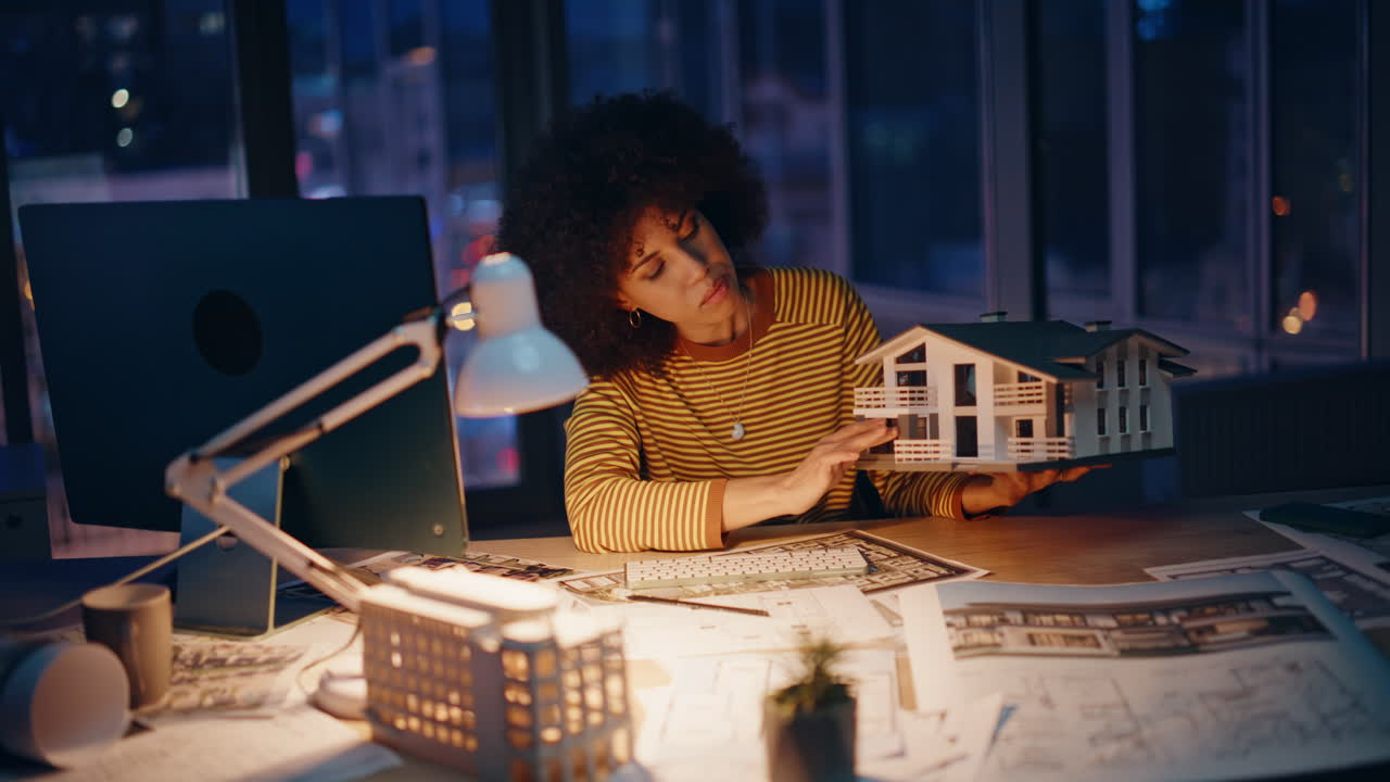 Designer oberato di lavoro progetta l'esterno di una casa, seduto di notte sul posto di lavoro. Donna stanca