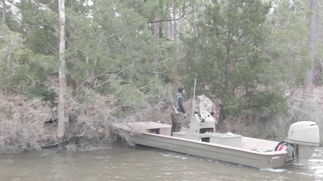 A hunter unloads gear from his camouflaged boat in a misty swamp, surrounded by mossy trees and calm waters, preparing for an adventurous day in the heart of the wilderness.
