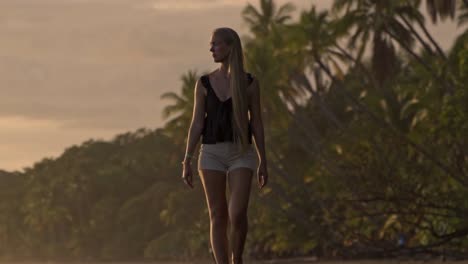 a serene moment as a woman walks barefoot along the golden shores of uvita beach during sunset, with the warm light casting long reflections on the wet sand and the jungle in the background