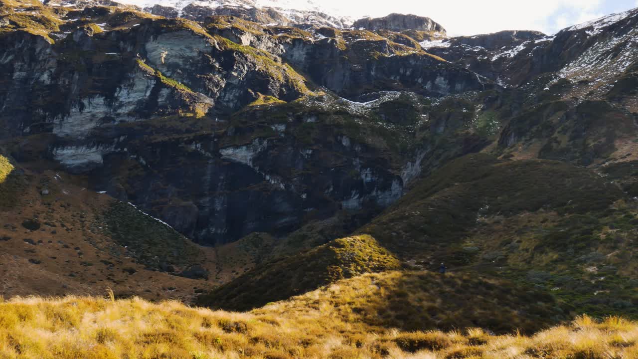 toma aérea de arriba hacia abajo de una excursionista caminando cuesta abajo por las montañas cubiertas de vegetación hacia el valle durante el día de verano