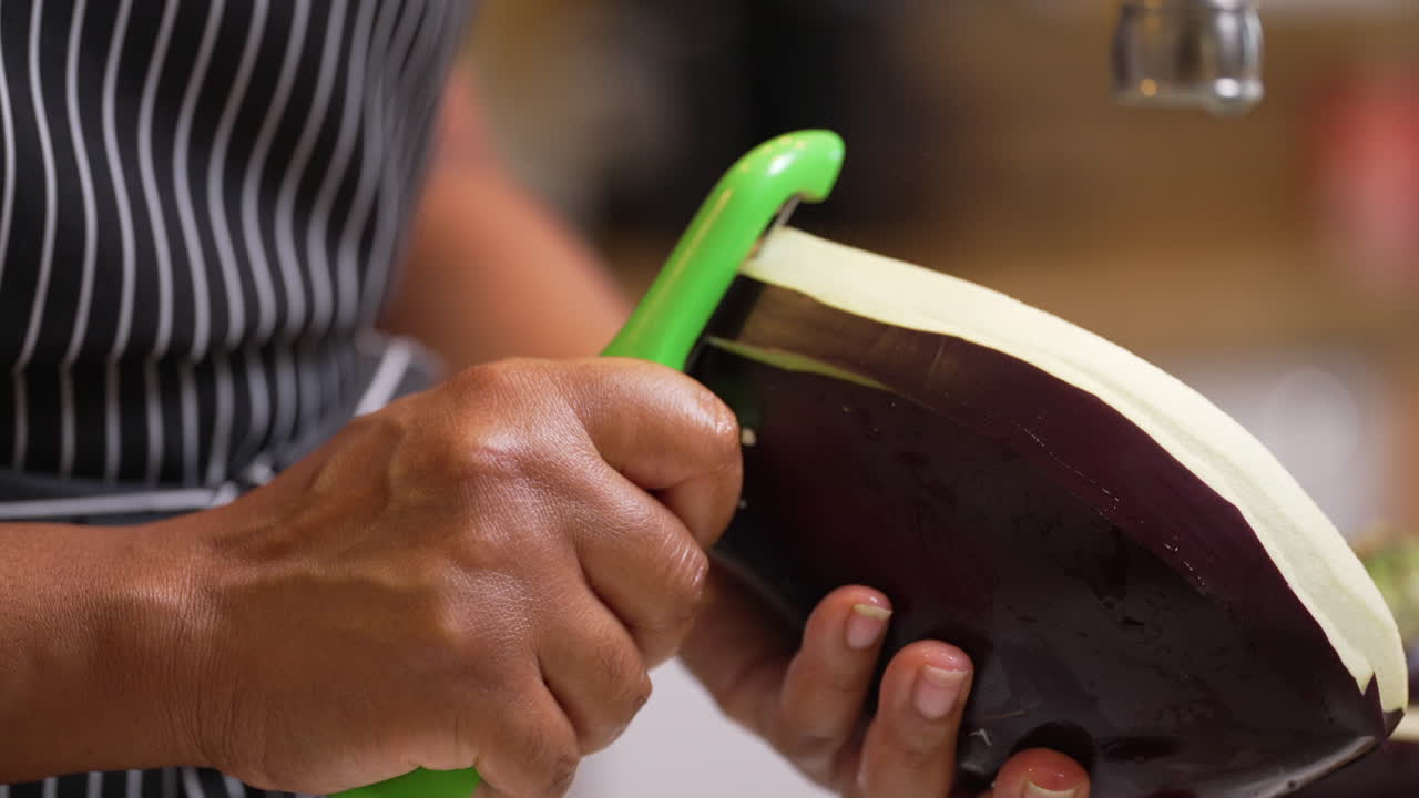 Black, African American hands seen peeling half of a large, raw eggplant - isolated slow motion
