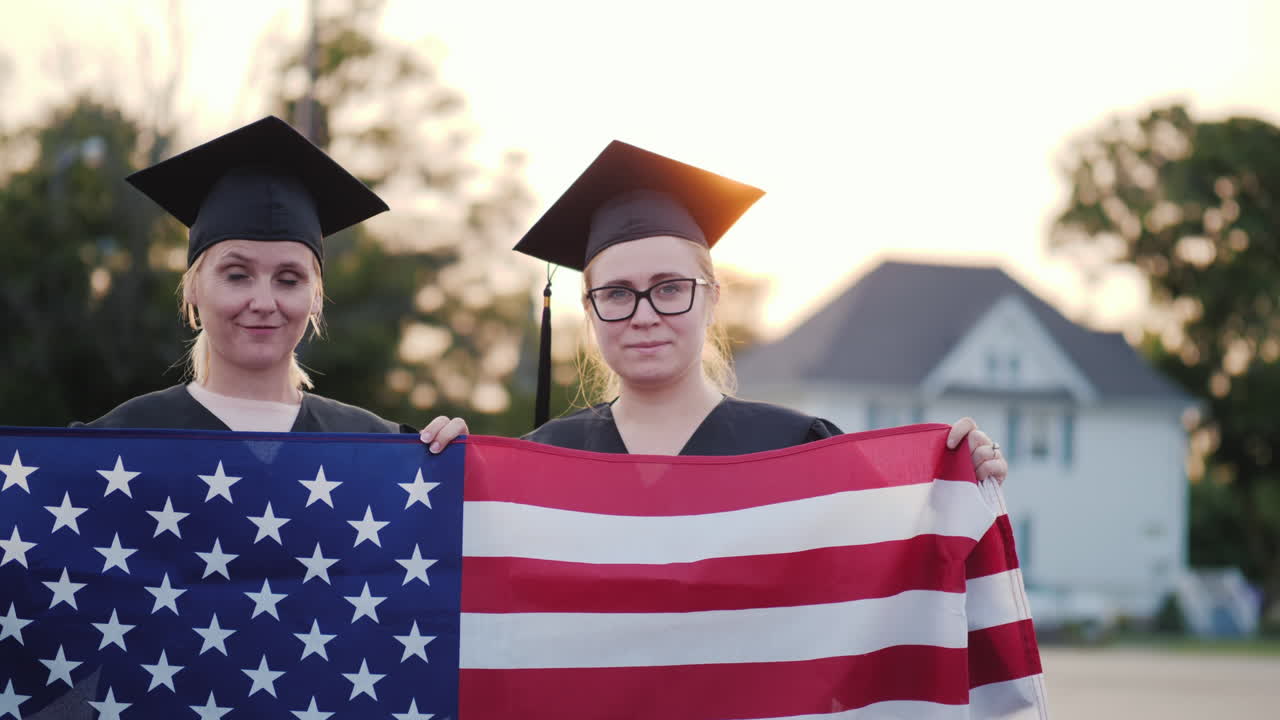 dos graduados universitarios en batas y gorras con la bandera americana