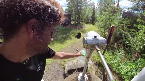 male filling up plastic water bottle from well in forest