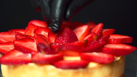 close up of a pastry chef placing the last strawberry on top of a custard cream filled tart