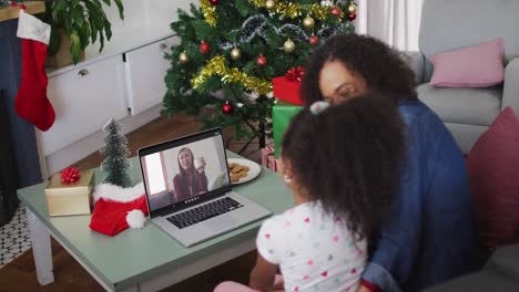 Happy-african-american-mother-and-daughter-on-video-call-on-laptop-with-female-friend-at-christmas