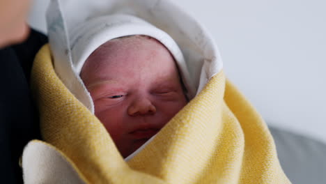 Face of a Caucasian newborn peeping out from the layer of wraps. Few hours-old baby in parent's hands. Close up.