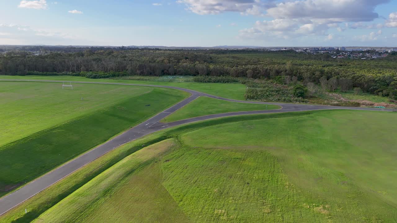 Aerial view of expansive green fields and pathways under clear skies at Gold Coast, Australia, captured by a drone