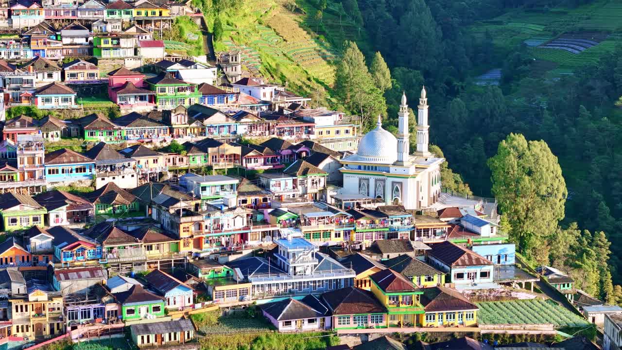 Aerial view of colorful hillside village with dense houses and a mosque surrounded by green mountains. Scenic rural architecture and landscape. Nepal Van Java, Mount Sumbing, Indonesia