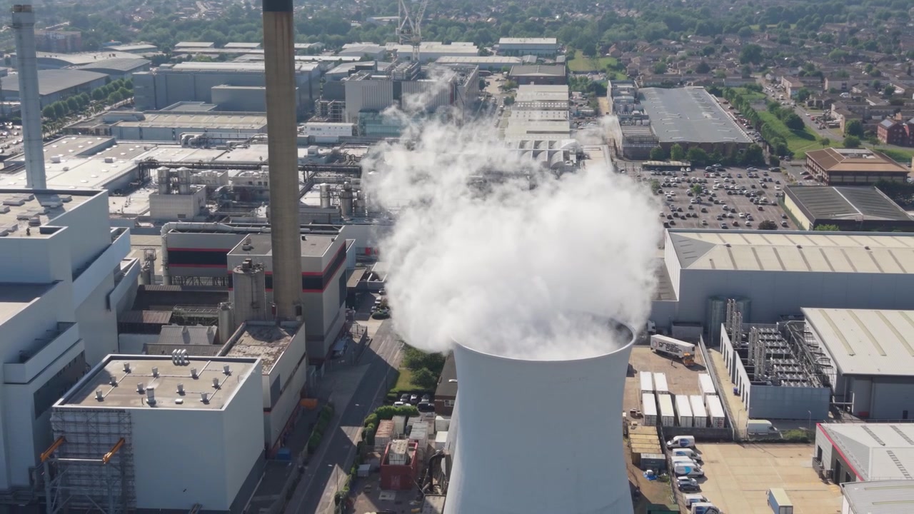 Una centrale elettrica multi-combustibile è operativa, generando energia dai rifiuti. Una torre di raffreddamento emette un grande pennacchio di vapore mentre altri edifici industriali e un'alta ciminiera sono in funzione in una giornata limpida e luminosa.