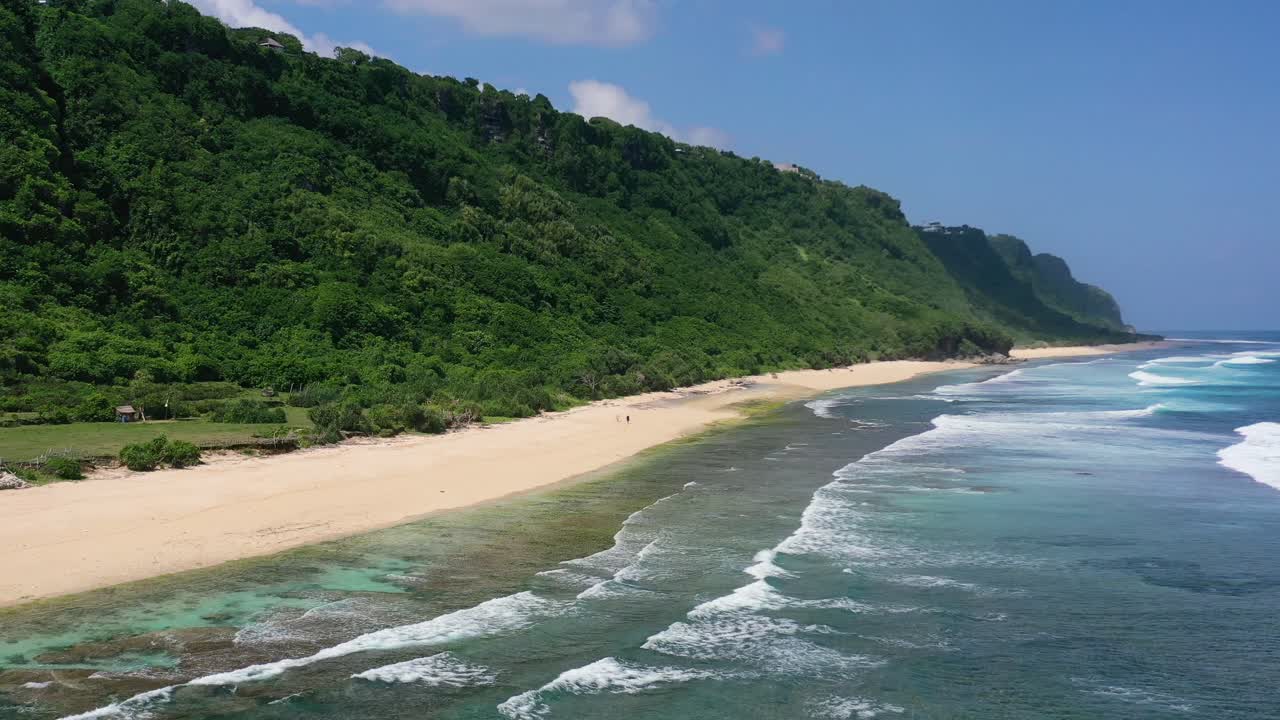 Onde oceaniche si infrangono sulla sabbia bianca deserta della spiaggia di Nyang Nyang a Uluwatu, Bali, con grandi scogliere montuose, vista aerea