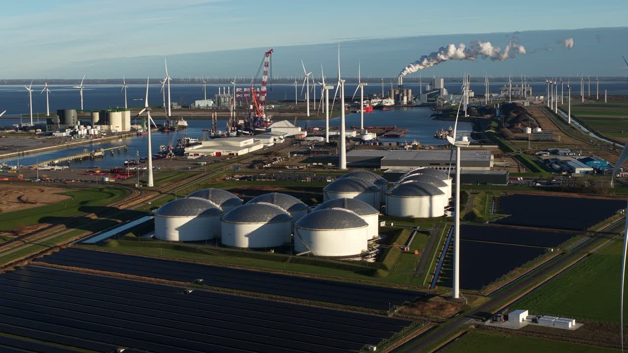 Aerial drone video of the Eemshaven industrial port, showing petroleum storage silos, industrial facilities, and large solar panel arrays next to ships, representing energy and logistics