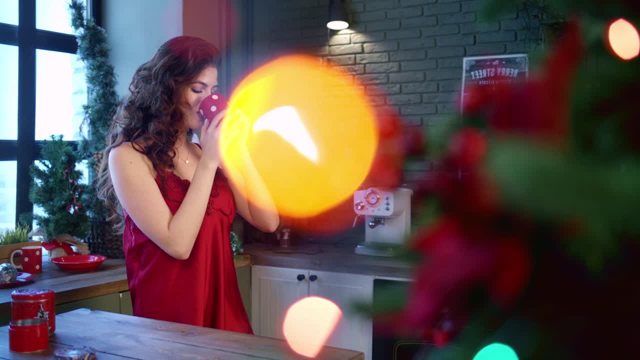A Joyful Moment During the Holidays: A Smiling Woman in a Red Dress Enjoys a Cozy Beverage Amidst Festive Decorations and Colorful Lights