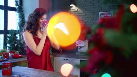 a joyful moment during the holidays: a smiling woman in a red dress enjoys a cozy beverage amidst festive decorations and colorful lights