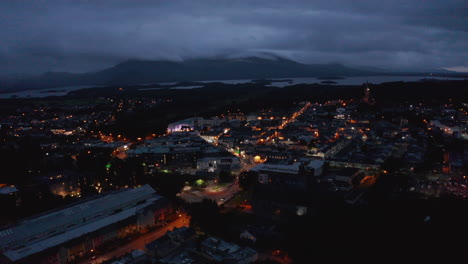 Fly-above-evening-town.-Low-traffic-in-orange-illuminated-streets.-Lake-and-mountains-shrouded-in-clouds-in-distance.-Killarney,-Ireland