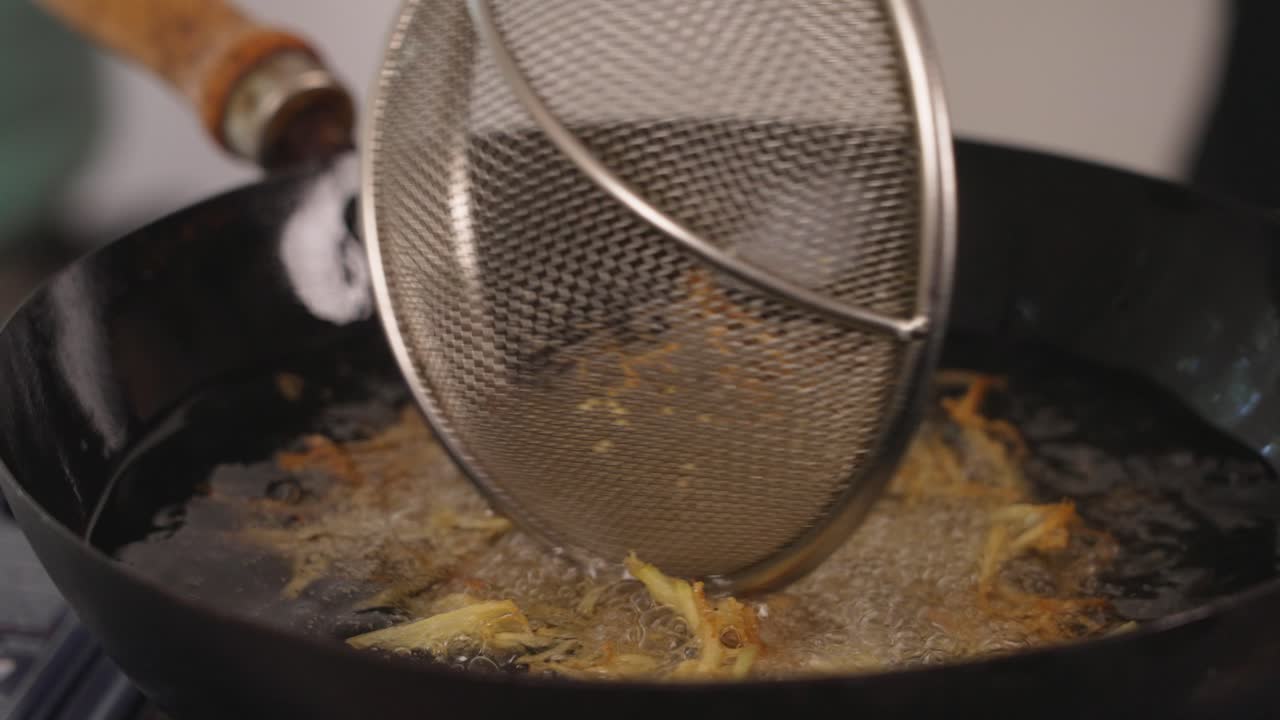 Nærbillede i slow motion af velsmagende og sprøde pai-kartofler, der friteres i varm olie; professionel kok bruger si til at blande og sikre, at alle overflader tilberedes jævnt