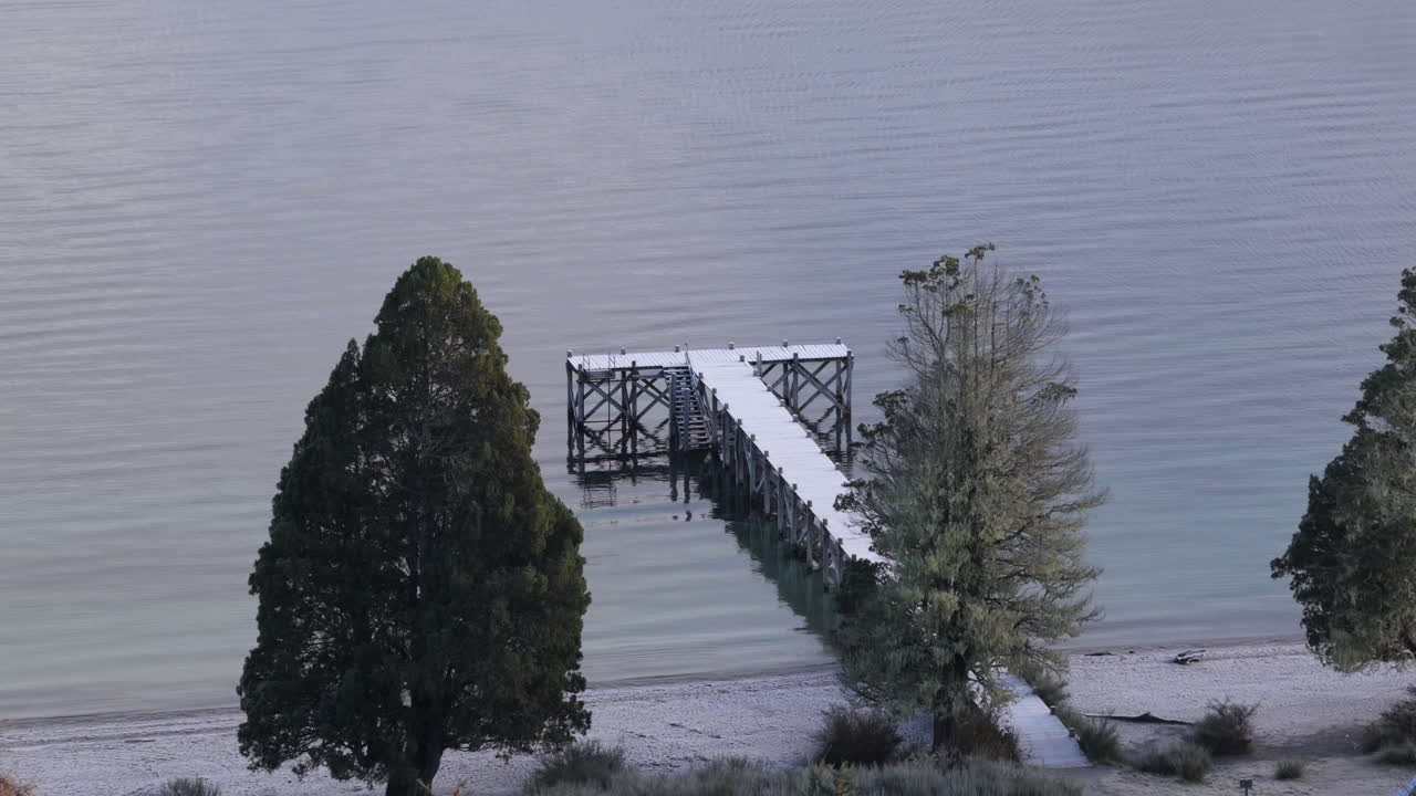 Pontile di legno che si estende dalla riva sabbiosa nelle acque limpide del Lago Espejo nel Parco Nazionale Nahuel Huapi vicino a Villa La Angostura, Provincia di Neuquén, Patagonia, Argentina, lento avvicinamento