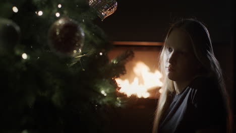 girl is sitting in the dark near a christmas tree, in the background a fire is burning in a fireplace. christmas eve