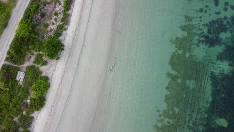 Er-Erhebt-Sich-über-Einem-Traditionellen-Fischerboot,-Das-An-Einem-Weißen-Sandstrand-Mit-Kristallklarem-Meerwasser-Auf-Einem-Idyllischen,-Abgelegenen-Tropischen-Inselparadies-Festgemacht-Ist