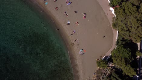 Drone-view-from-above-of-a-beautiful-beach-with-turquoise-water-with-people-sunbathing-and-playing,-in-Costa-Brava,-Catalunya,-Spain
