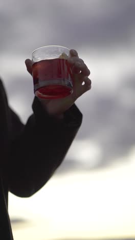 hand houdt een rood drankje, witte bewolkte achtergrond kopieer ruimte langzame beweging