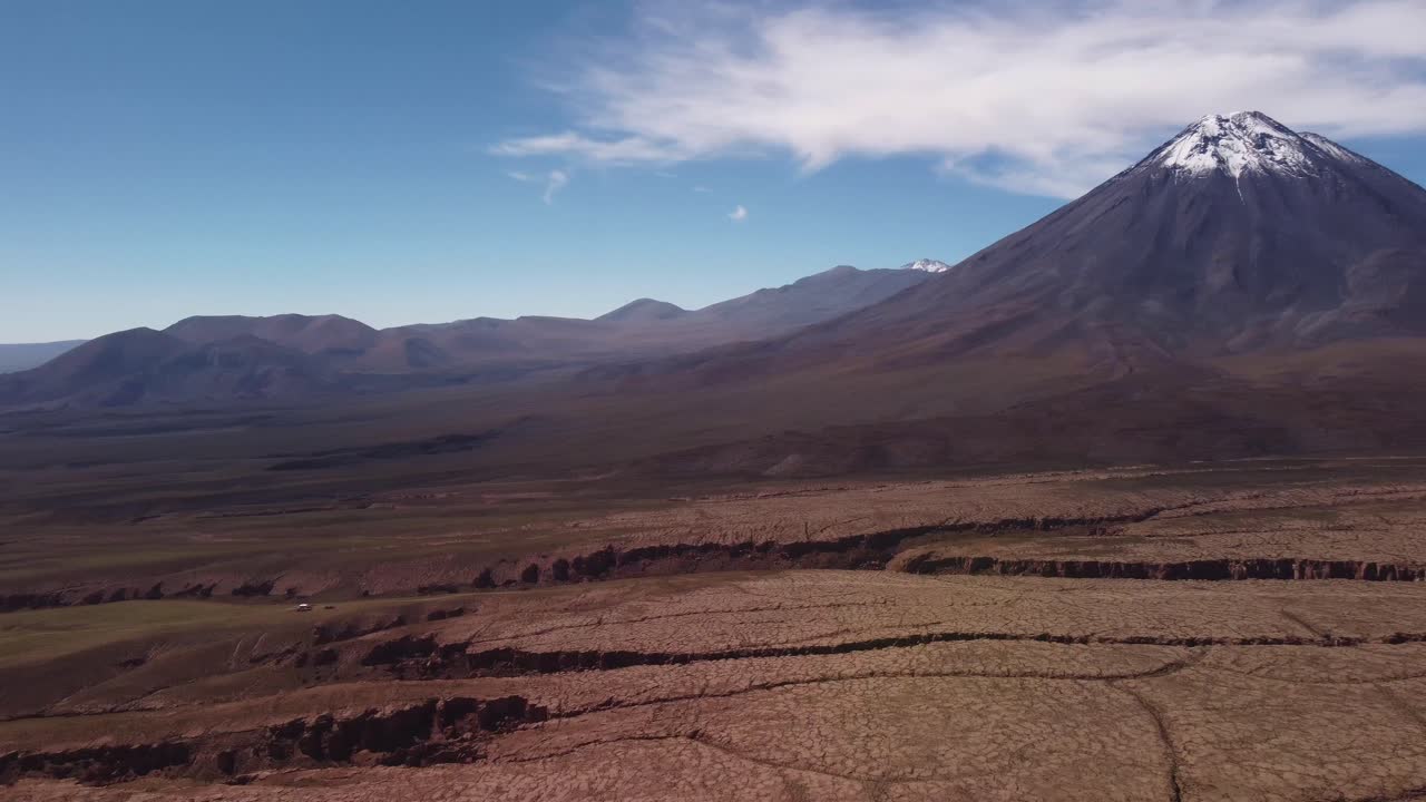 Dramatic drone footage of Licancabur Volcano near San Pedro de Atacama at the Chile–Bolivia border. Harsh desert meets snow-capped peaks in the Andean altiplano.