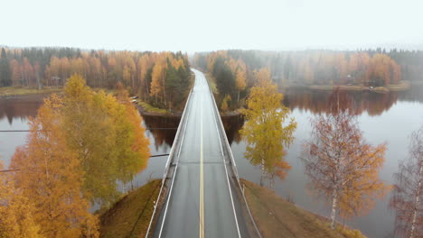 aerial, decreasing, drone shot, above a bridge, surrounded by mist and autumn colors,, on a foggy, misty and cloudy, fall day, at lake pielinen, in nurmes, north karelia, finland