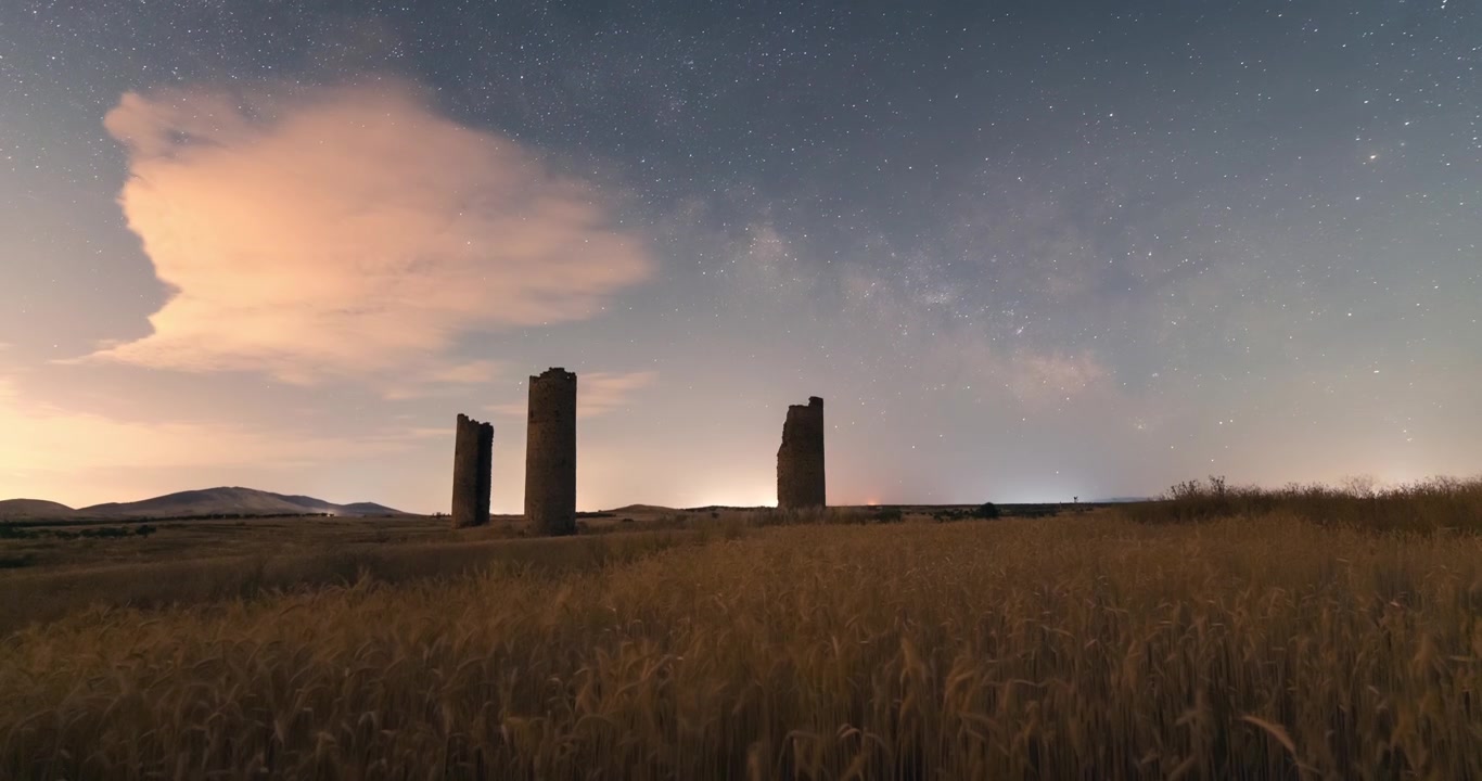 Gult vetefält, skörd av spannmålsgrödor och Galvez slotts torn under natt-timelapse med Vintergatan som stiger på en stjärnhimmel.