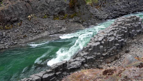 slow-motion establishing shot of green-water river flowing in spectacular basalt canyon in iceland