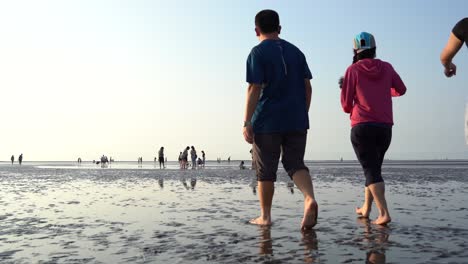 Tourists-walking-barefoot-on-muddy-tidal-flats,-experiencing-the-nature-on-tranquil-afternoon-with-beautiful-water-reflection-on-the-ground-at-Gaomei-wetland-preservation-area,-Taichung