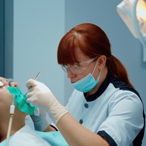 professional dentist treats patient's teeth. woman sitting in a dental chair with opened mouth in modern stomatology office. nurse gives instruments to a doctor.